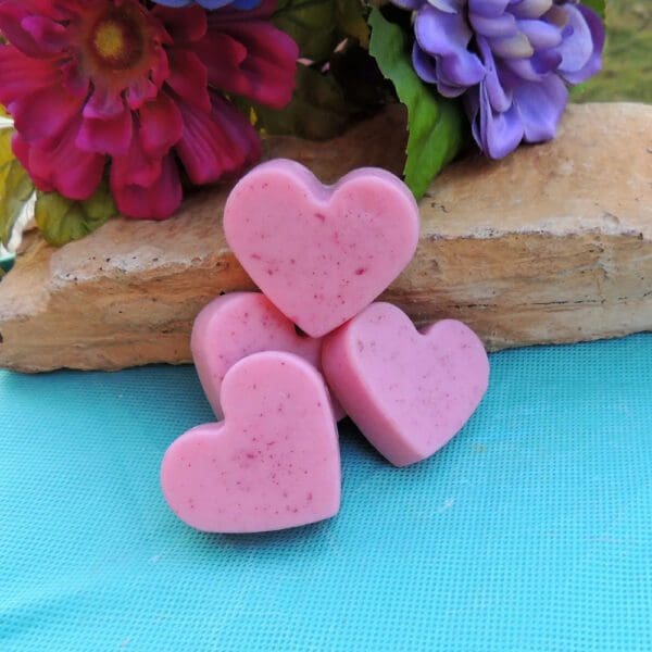 Four pink heart-shaped soaps on blue surface.